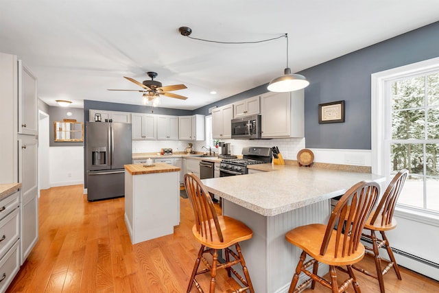 kitchen featuring sink, a breakfast bar area, appliances with stainless steel finishes, decorative light fixtures, and kitchen peninsula