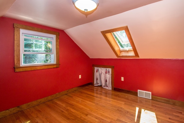 additional living space featuring vaulted ceiling with skylight and light hardwood / wood-style floors