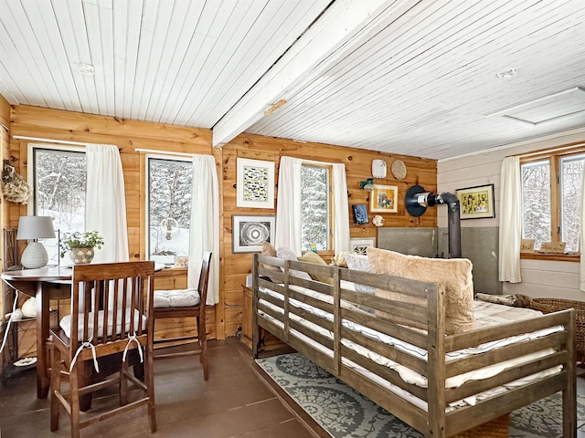 interior space with beamed ceiling, wood walls, multiple windows, and a wood stove