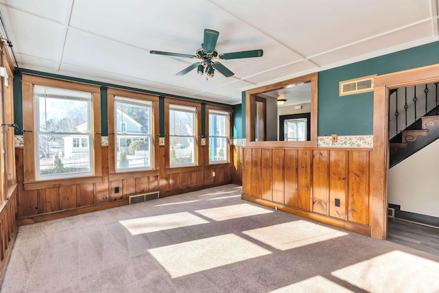 interior space featuring light colored carpet, ceiling fan, and wood walls