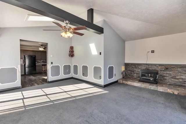 unfurnished living room featuring ceiling fan, dark colored carpet, lofted ceiling with beams, a textured ceiling, and a wood stove