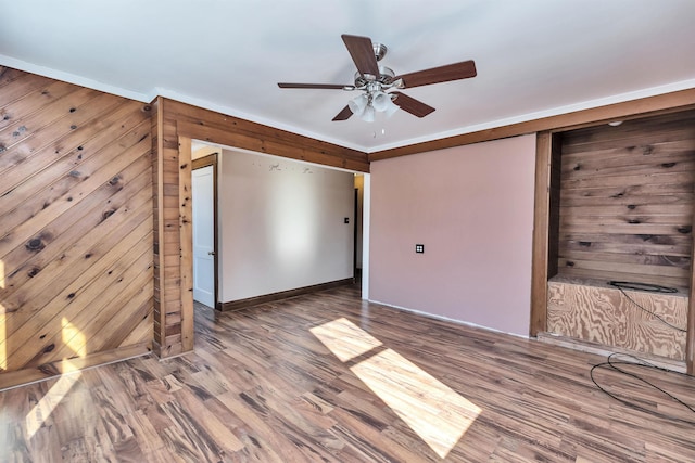 empty room with hardwood / wood-style flooring, crown molding, ceiling fan, and wood walls