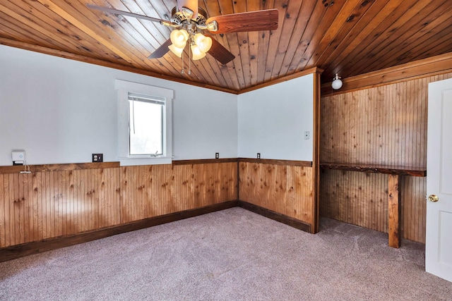 carpeted empty room featuring wood ceiling, ceiling fan, ornamental molding, and wooden walls