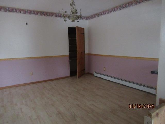 empty room featuring hardwood / wood-style floors, a notable chandelier, and baseboard heating