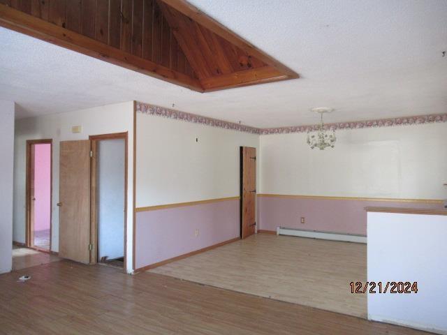 unfurnished room with a baseboard heating unit, wood-type flooring, a chandelier, and vaulted ceiling