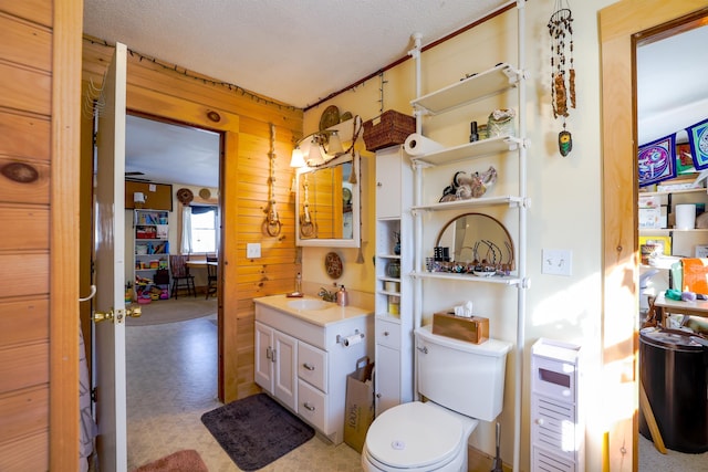 bathroom with vanity, a textured ceiling, wooden walls, and toilet