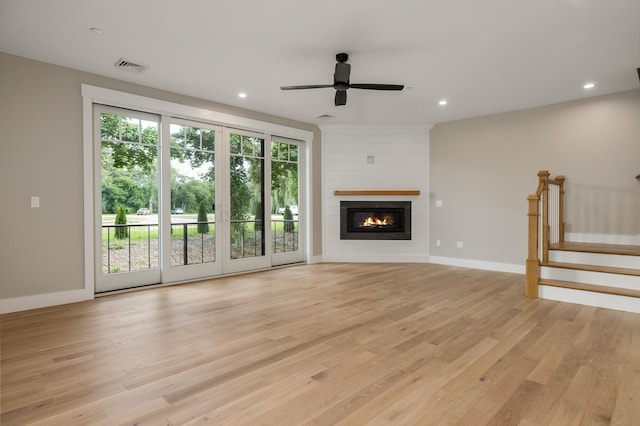 unfurnished living room with ceiling fan, a large fireplace, and light wood-type flooring