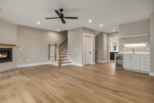 unfurnished living room with sink, a fireplace, light hardwood / wood-style floors, and beverage cooler