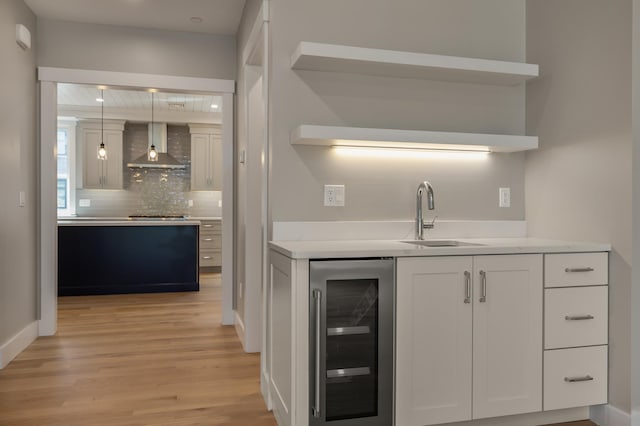 kitchen featuring decorative light fixtures, white cabinetry, sink, beverage cooler, and wall chimney exhaust hood