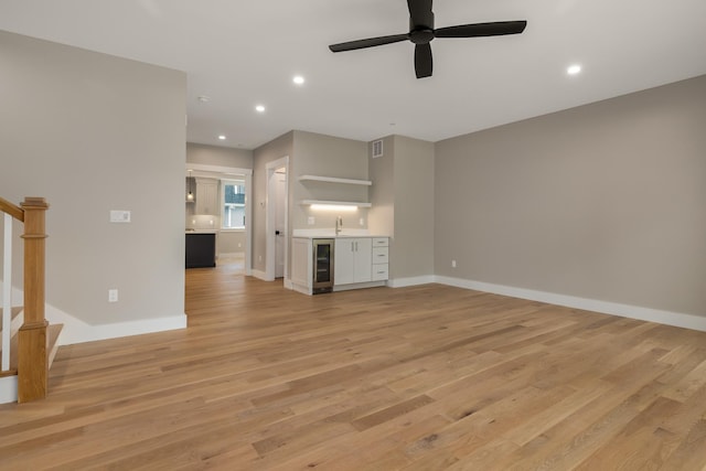 unfurnished living room with ceiling fan, indoor wet bar, wine cooler, and light wood-type flooring