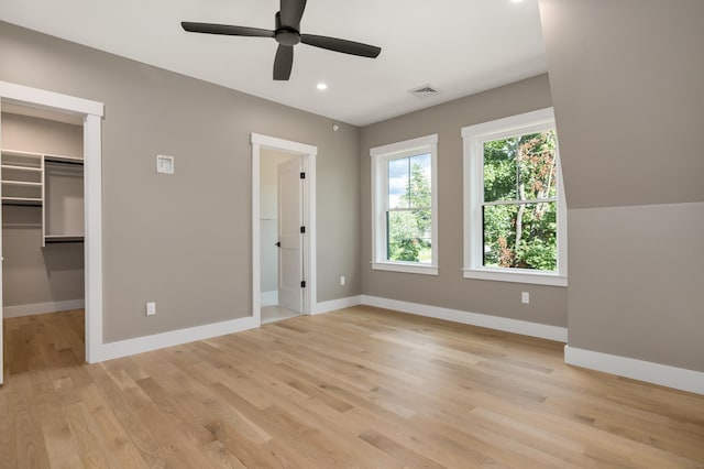 unfurnished bedroom featuring a spacious closet, light hardwood / wood-style flooring, a closet, and ceiling fan