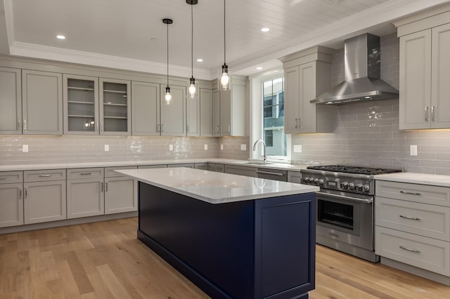 kitchen with wall chimney range hood, stainless steel stove, hanging light fixtures, a center island, and light wood-type flooring