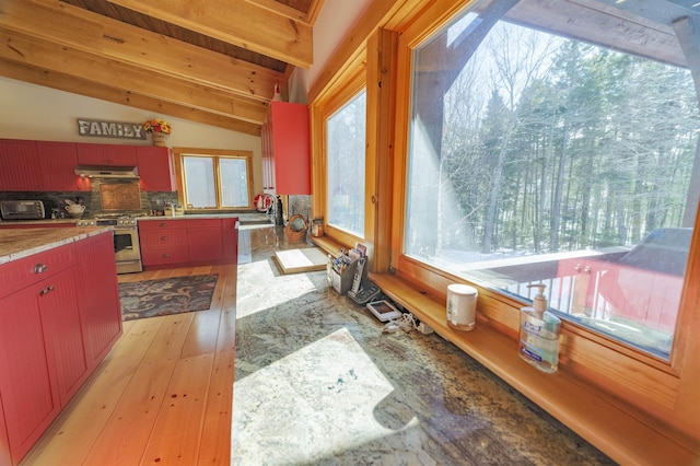 kitchen with vaulted ceiling with beams, backsplash, stainless steel gas range oven, and light hardwood / wood-style floors