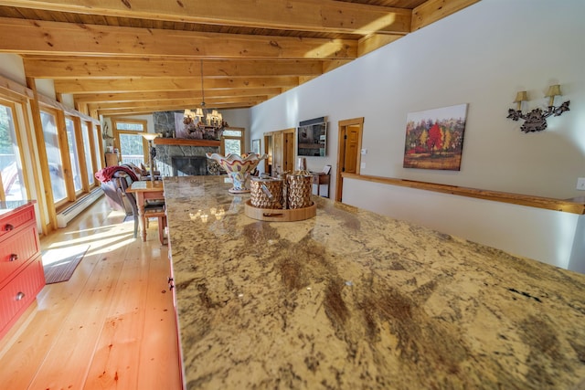 interior space with a stone fireplace, vaulted ceiling with beams, a chandelier, wood ceiling, and light hardwood / wood-style flooring