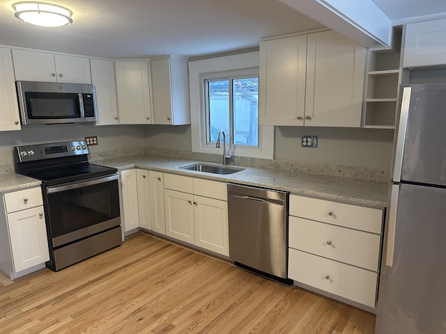 kitchen with sink, light stone counters, light wood-type flooring, stainless steel appliances, and white cabinets