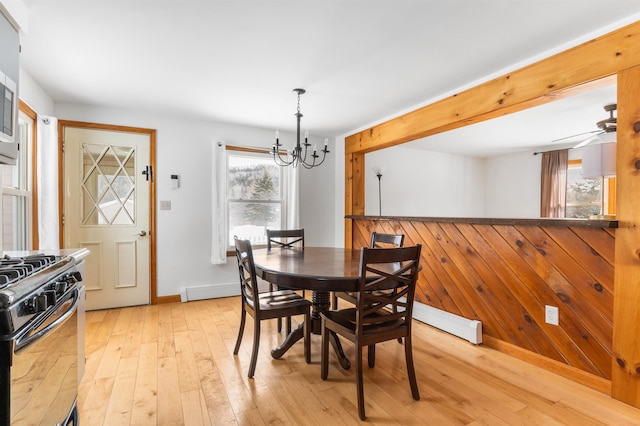 dining room featuring ceiling fan with notable chandelier, light hardwood / wood-style floors, and wood walls