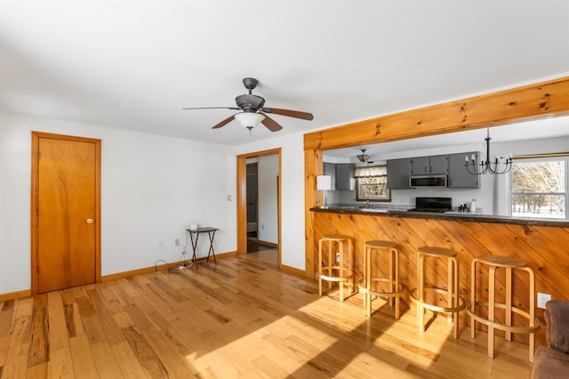 kitchen with gray cabinets, ceiling fan with notable chandelier, wood-type flooring, stove, and kitchen peninsula