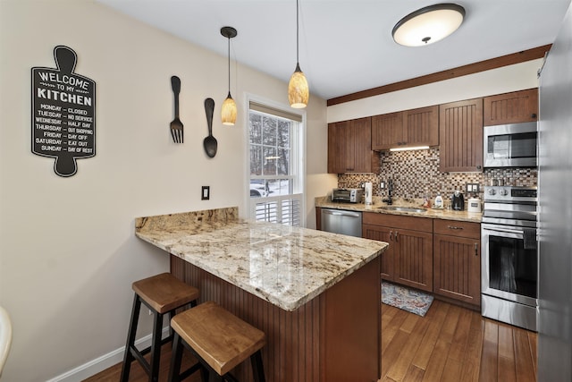 kitchen featuring a kitchen bar, tasteful backsplash, kitchen peninsula, pendant lighting, and stainless steel appliances