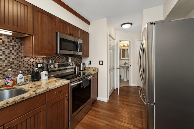 kitchen featuring sink, stainless steel appliances, dark hardwood / wood-style floors, tasteful backsplash, and light stone counters