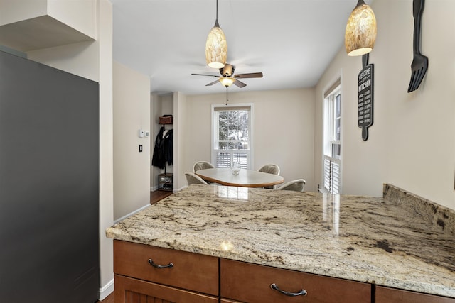 kitchen featuring ceiling fan, refrigerator, decorative light fixtures, and light stone countertops