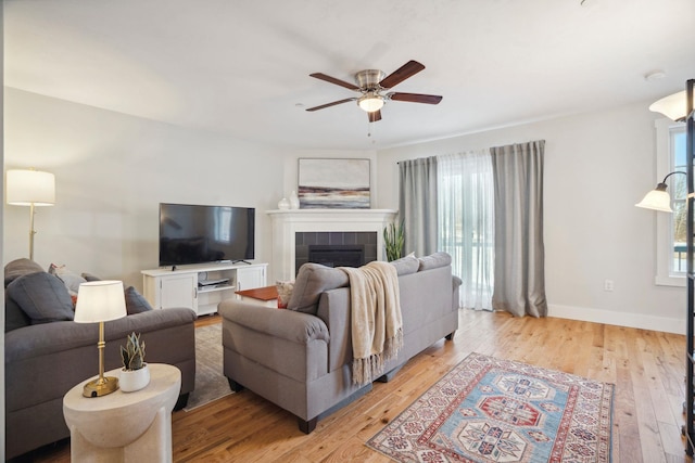 living room with a tiled fireplace, ceiling fan, and light wood-type flooring