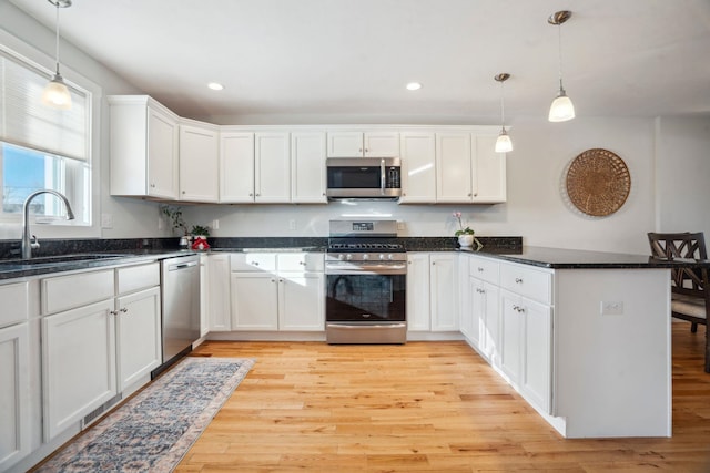 kitchen featuring white cabinetry, stainless steel appliances, decorative light fixtures, and sink