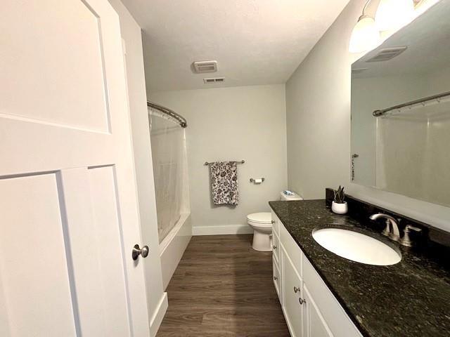 full bathroom with hardwood / wood-style flooring, vanity, shower / bathtub combination with curtain, and toilet