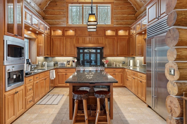 kitchen with pendant lighting, decorative backsplash, dark stone counters, a center island, and built in appliances