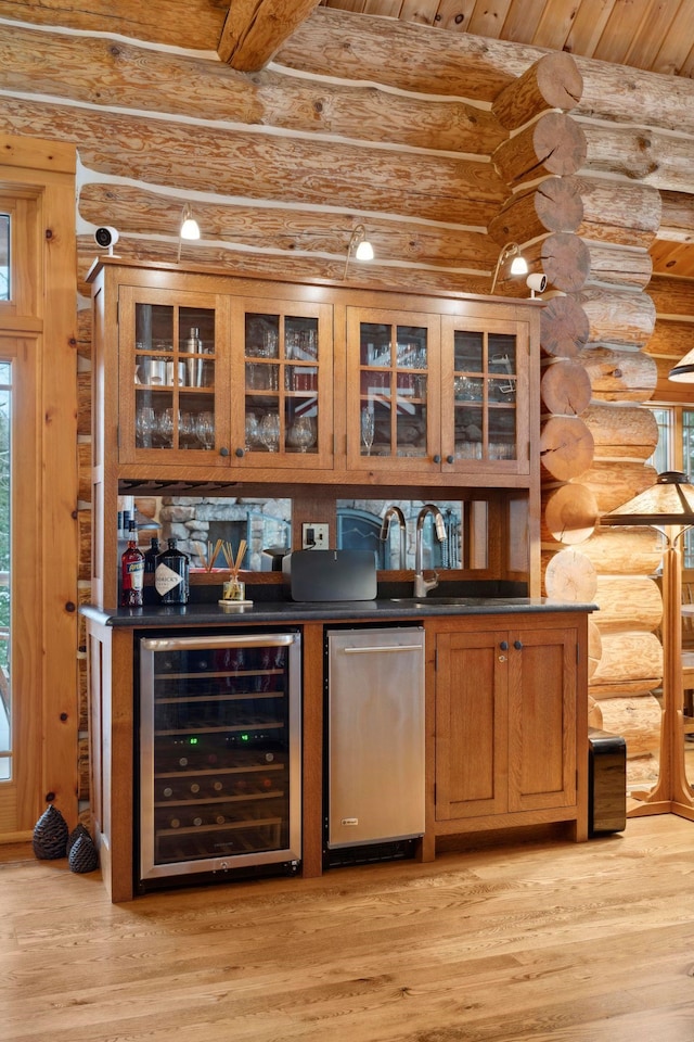 bar featuring fridge, beverage cooler, log walls, and light wood-type flooring