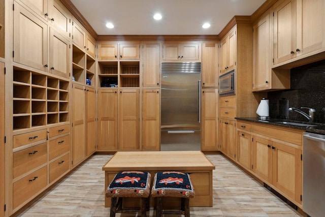 kitchen featuring built in appliances, light brown cabinetry, and dark stone counters