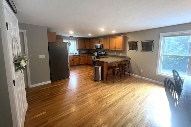 kitchen featuring a kitchen bar, light wood-type flooring, kitchen peninsula, and appliances with stainless steel finishes