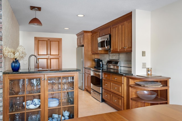 kitchen with light tile patterned flooring, decorative light fixtures, appliances with stainless steel finishes, dark stone counters, and decorative backsplash