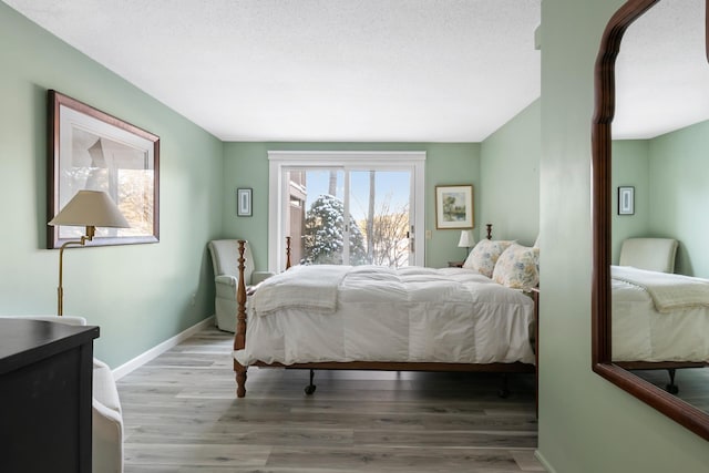 bedroom featuring access to exterior, light hardwood / wood-style floors, and a textured ceiling