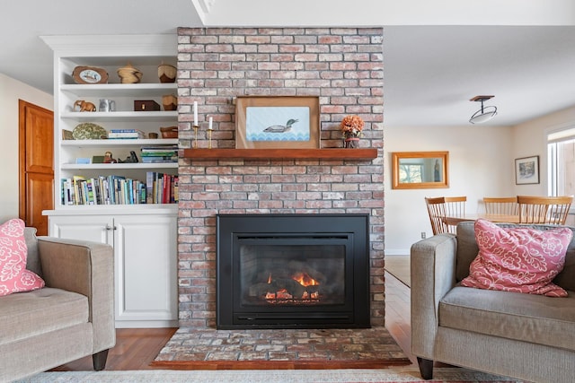 living room featuring hardwood / wood-style flooring, built in shelves, and a brick fireplace