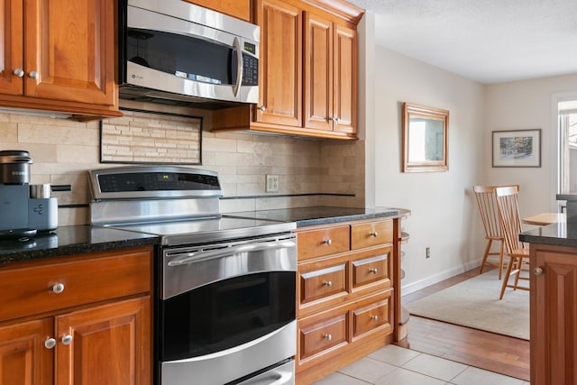 kitchen featuring dark stone countertops, backsplash, light tile patterned floors, and stainless steel appliances