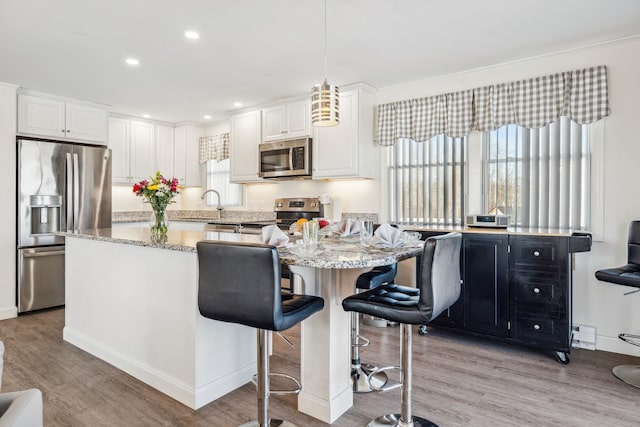 kitchen with white cabinetry, hanging light fixtures, stainless steel appliances, light stone countertops, and light hardwood / wood-style flooring