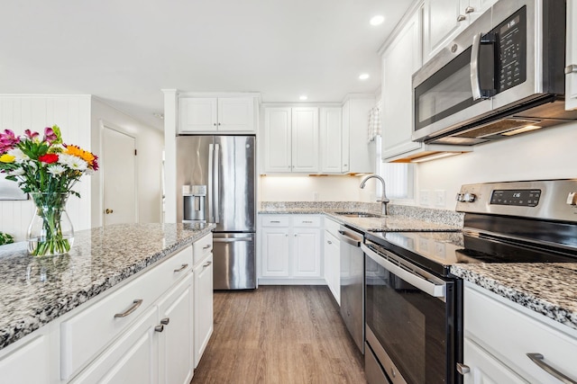 kitchen featuring sink, light hardwood / wood-style flooring, white cabinetry, stainless steel appliances, and light stone countertops