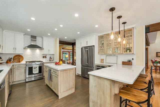 kitchen featuring wall chimney exhaust hood, a center island, appliances with stainless steel finishes, a kitchen breakfast bar, and pendant lighting