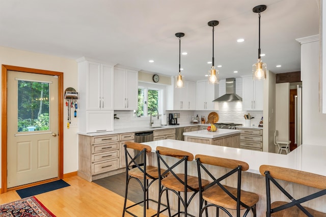 kitchen featuring a kitchen island, wall chimney range hood, white cabinets, and a kitchen breakfast bar