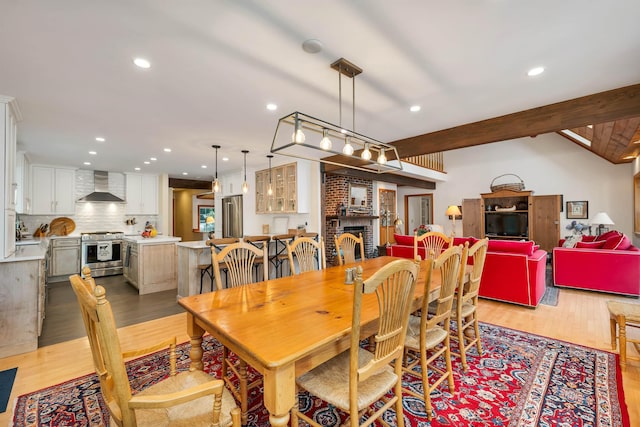 dining room with a brick fireplace, light hardwood / wood-style flooring, and lofted ceiling with beams