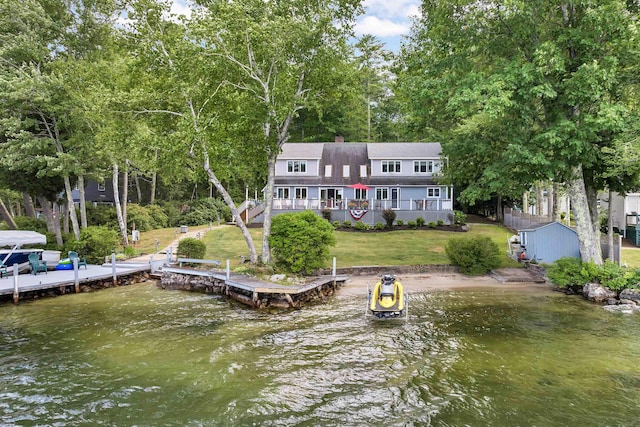 back of property with a deck with water view, a lawn, and a storage unit