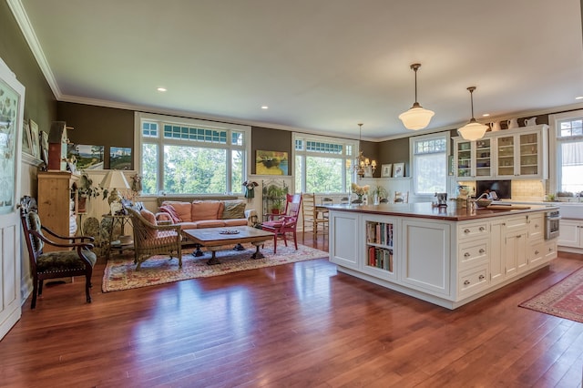 kitchen with decorative light fixtures, white cabinetry, an island with sink, ornamental molding, and dark wood-type flooring