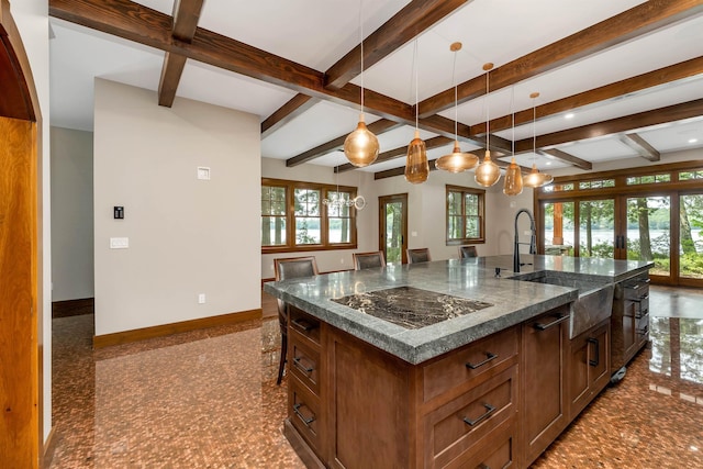 kitchen with hanging light fixtures, a kitchen island with sink, dark stone countertops, and black electric cooktop