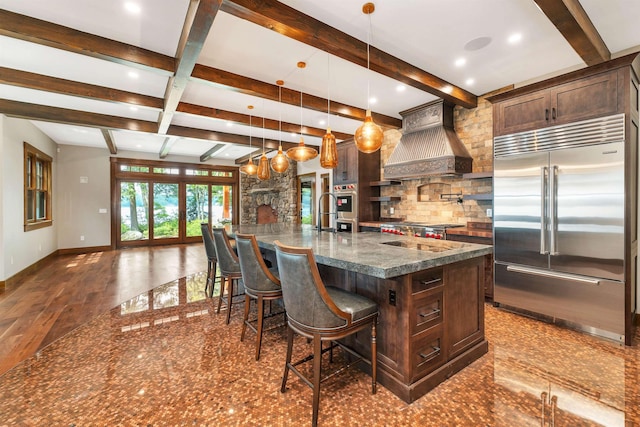 kitchen featuring a breakfast bar area, a large island with sink, appliances with stainless steel finishes, custom range hood, and pendant lighting