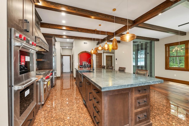 kitchen with pendant lighting, high quality appliances, beamed ceiling, sink, and a large island with sink