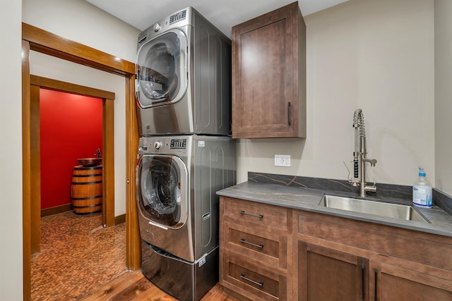 clothes washing area featuring cabinets, stacked washer / dryer, sink, and wood-type flooring