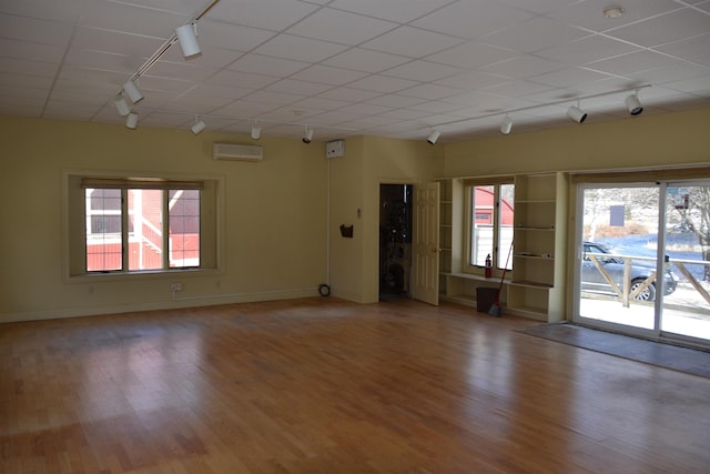 empty room with a wall mounted air conditioner, hardwood / wood-style floors, and rail lighting