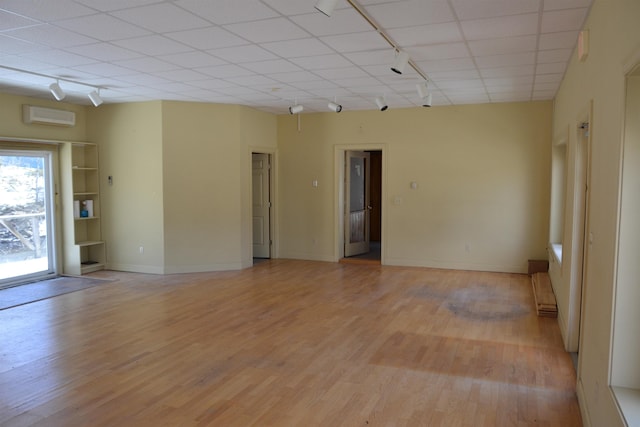 empty room featuring a wall mounted air conditioner, track lighting, and light hardwood / wood-style floors