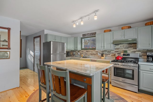 kitchen with appliances with stainless steel finishes, a breakfast bar area, backsplash, a center island, and light stone counters