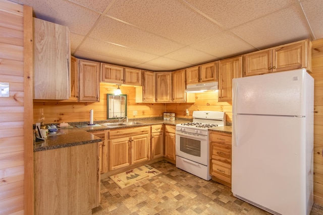 kitchen featuring light brown cabinetry, sink, wooden walls, white appliances, and a drop ceiling